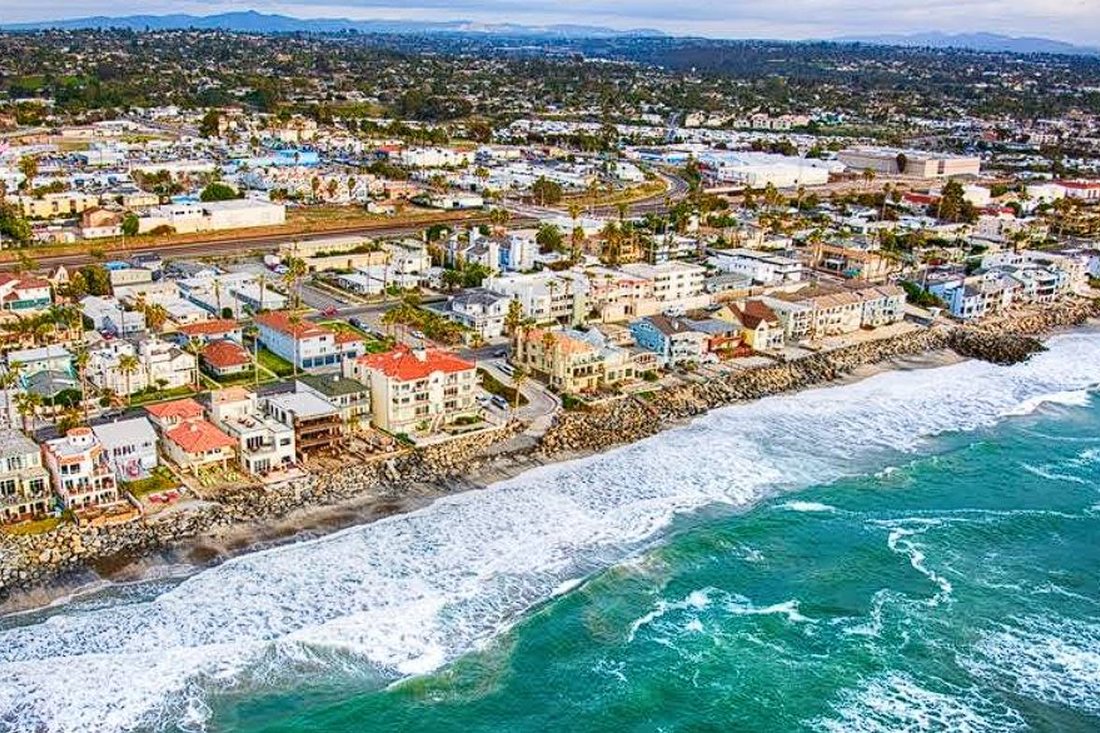 Aerial view of light-colored homes lining the beach and surf in north San Diego County