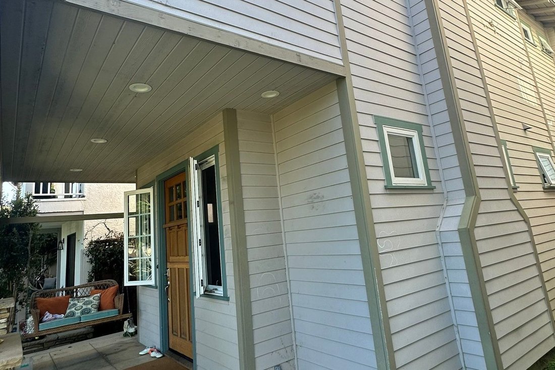 Pale gray lap siding with sage-green trim and a wood front door under a covered entry, from a Lifetime Custom Painting project in Coronado