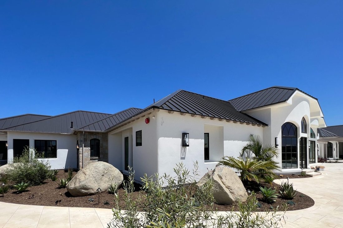 White single-story stucco home with a dark metal roof and desert landscaping