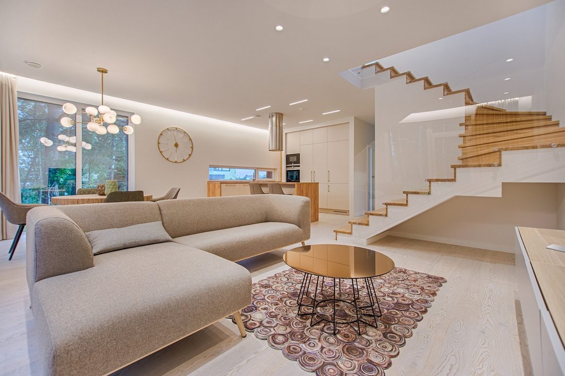 Open-plan living room with warm white walls, a beige sectional sofa and a wood staircase