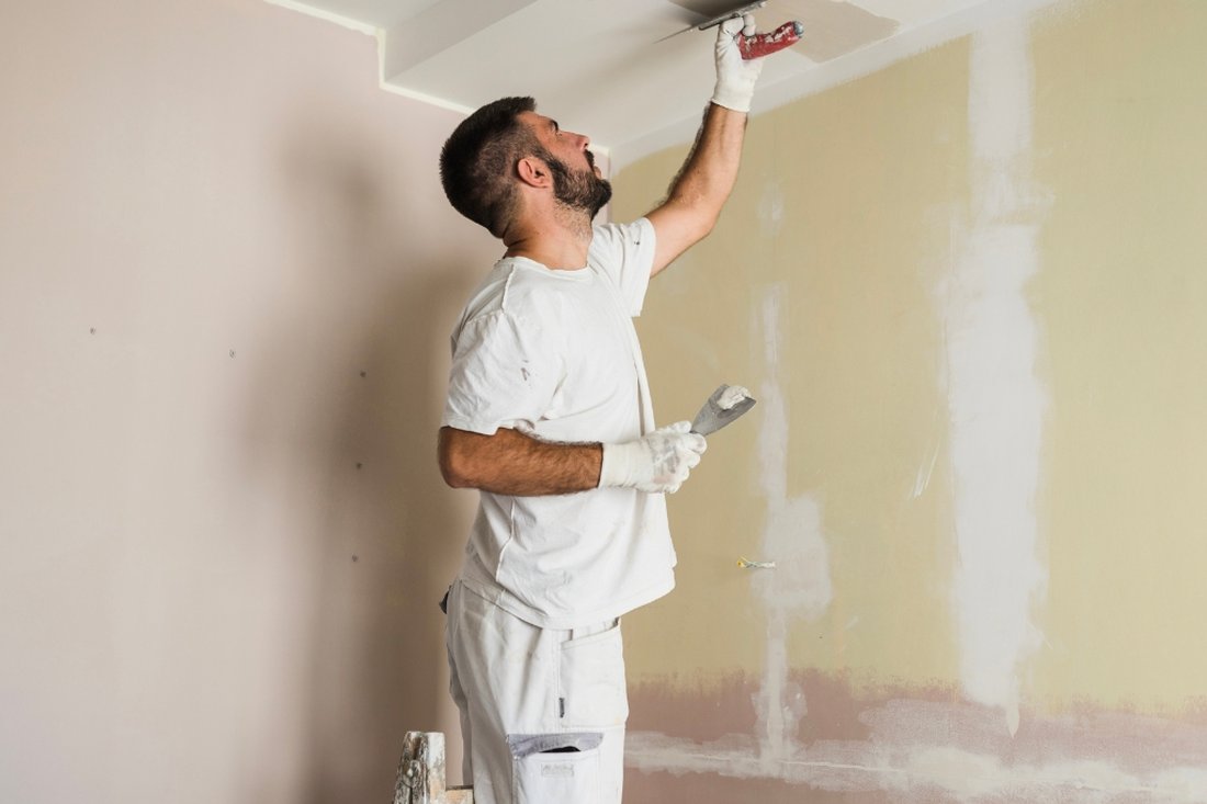Worker using a putty knife on a patched wall, with drywall compound visible over old paint
