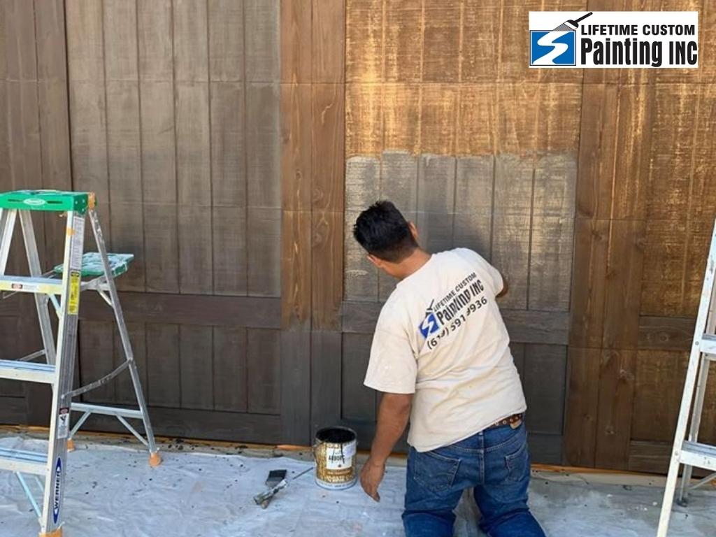 A painter staining the wooden fence